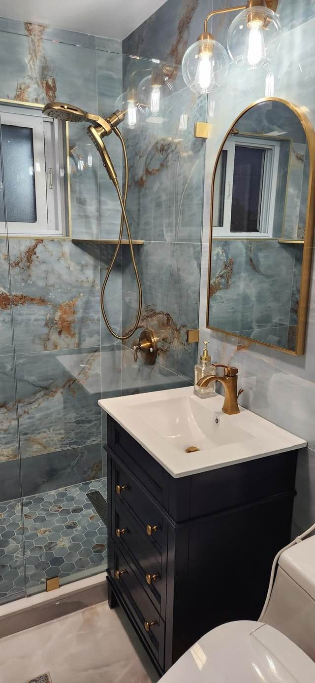 Blue onyx marble tile shower with brass fixtures, arched gold mirror, and dark blue vanity