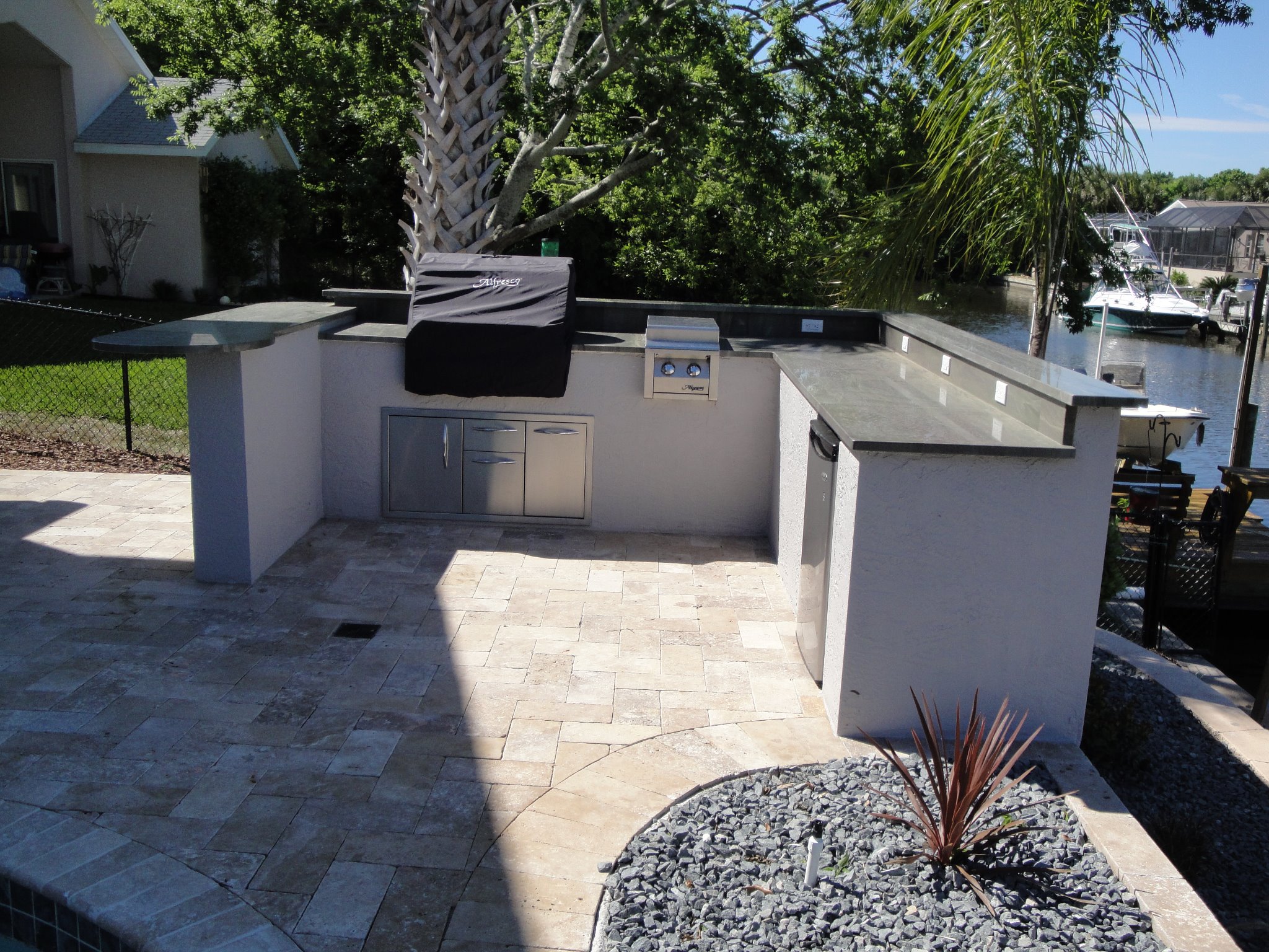 Waterfront summer kitchen in Palm Coast with travertine paver patio, built-in grill, and stainless storage overlooking a canal