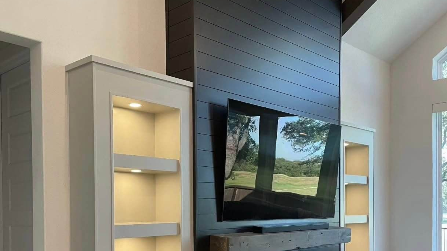 Black shiplap TV accent wall with mounted flat screen, built-in LED-lit shelving niches, and reclaimed wood mantel