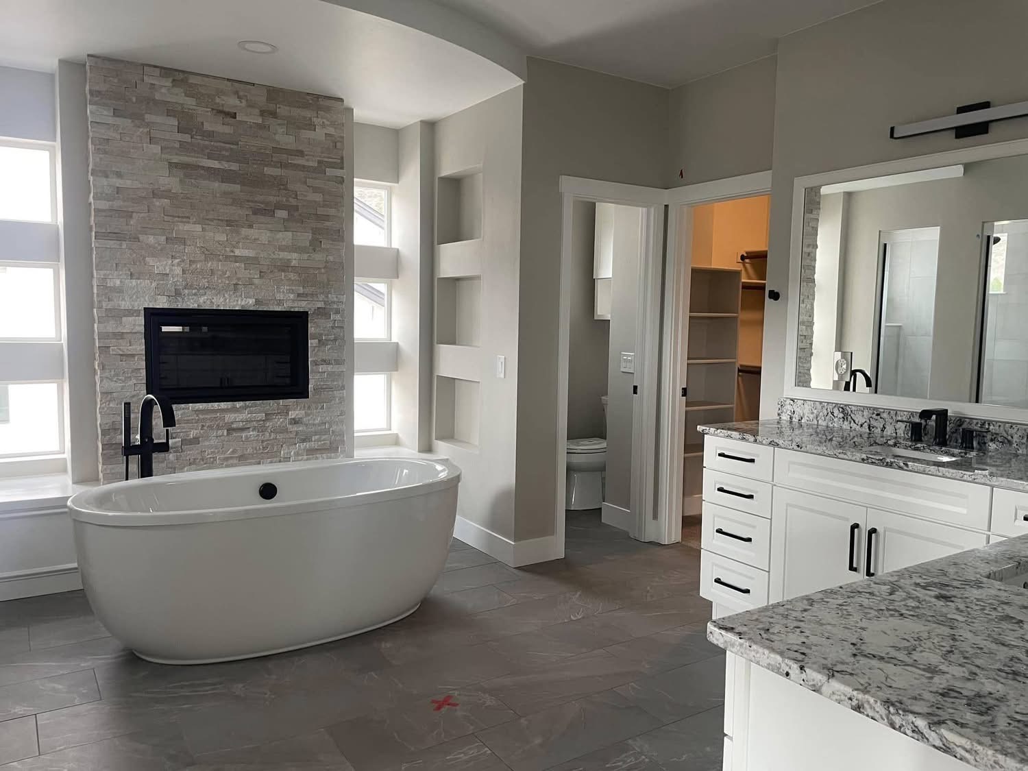 Luxury master bathroom remodel in Palm Coast with stacked stone fireplace wall, freestanding tub, granite vanity, and porcelain tile floor by Jeff Handyman